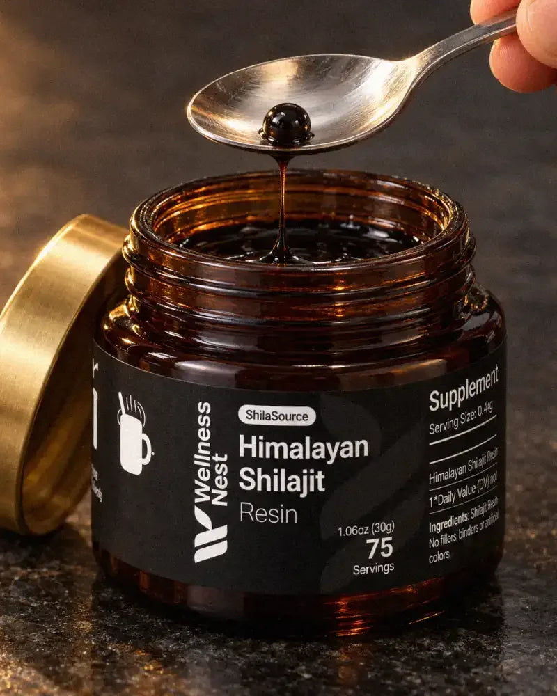 The open ShilaSource jar with its gold lid beside it and a steel teaspoon holding one pea-sized bead of black resin, a strand still joining it to the jar