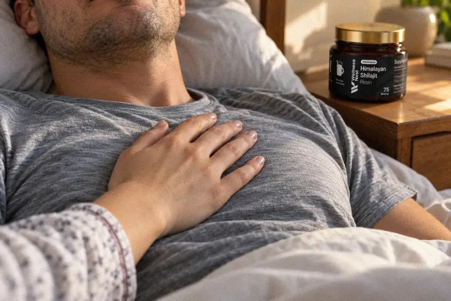 A woman's hand rests on a man's chest in a bed in the morning sun, the ShilaSource jar on the nightstand